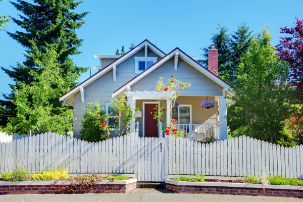 Grey small cute house with white fence and gates.